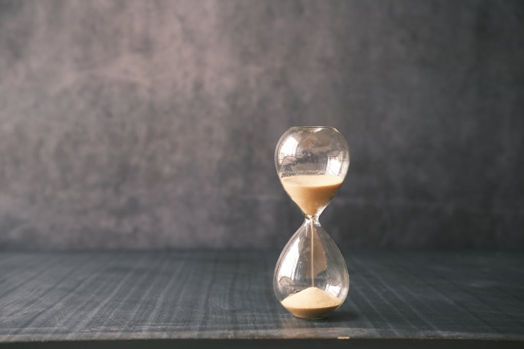 A close-up of a classic hourglass with sand slowly passing through, set against a textured background.