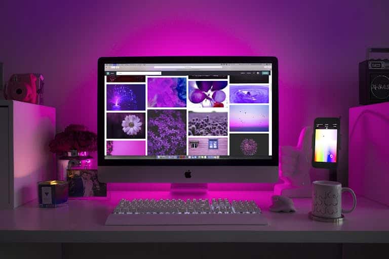 Modern desk setup with neon lighting and a desktop computer displaying colorful images.