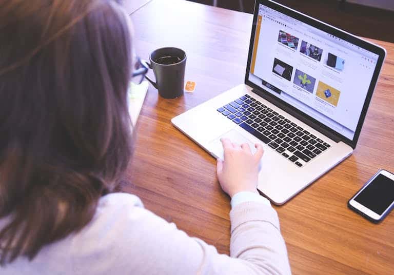 Person browsing the web on a MacBook at a wooden desk with a smartphone.